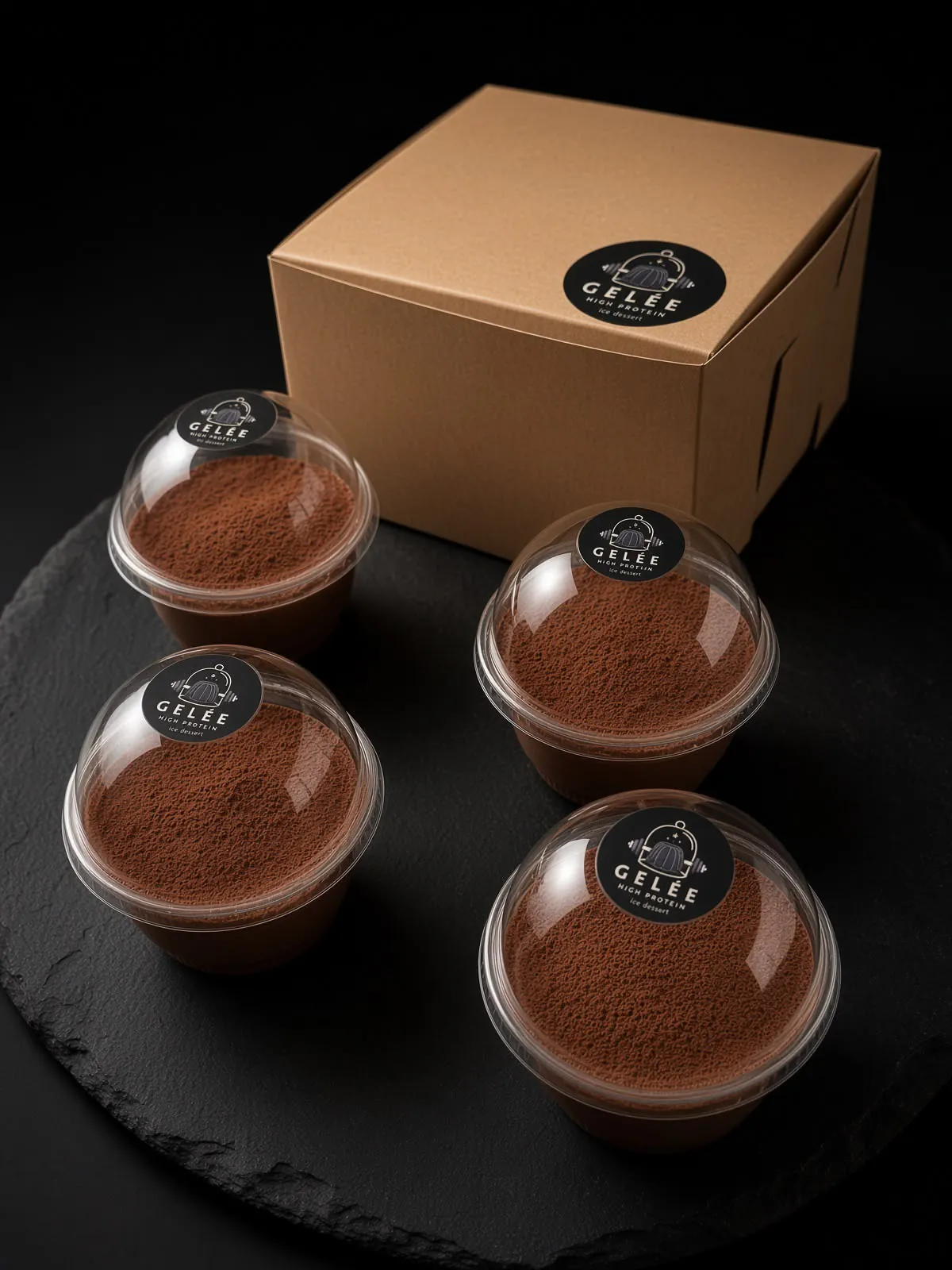 Cuatro gelées altos en proteína sabor chocolate, espolvoreados con cacao, sobre una pizarra y frente a la caja de la marca